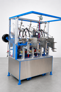 Industrial automatic manufacturing machine with a blue frame, stainless steel panels and an array of tubes and actuators inside a clear enclosure.
