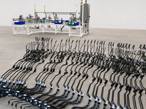 Row of black curved tubes laid out on a concrete floor, with an assembly station and machinery in the background.