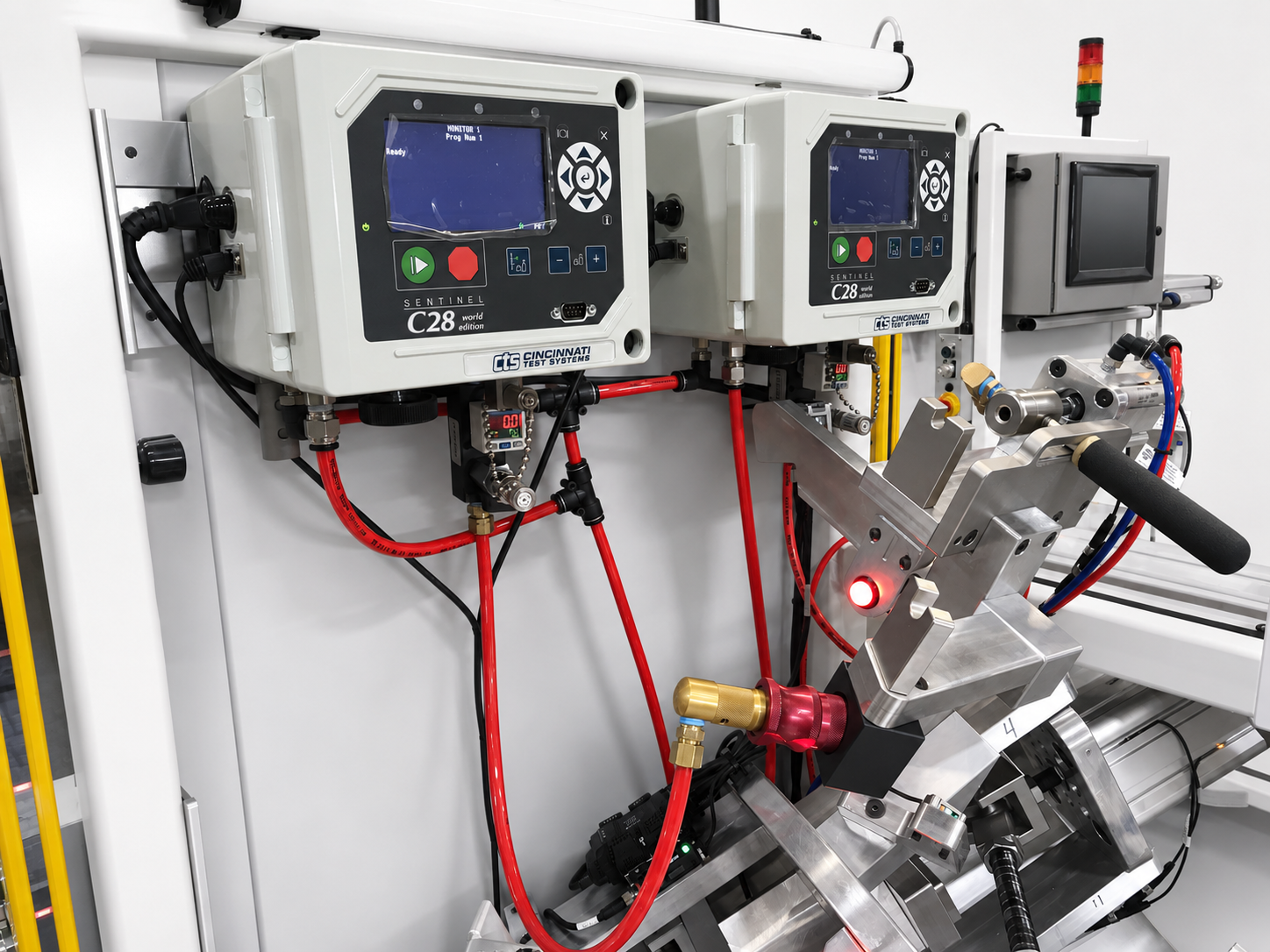 Industrial test rig with two SENTINEL C28 control panels, red hoses, and a metal gripping/assembly head.