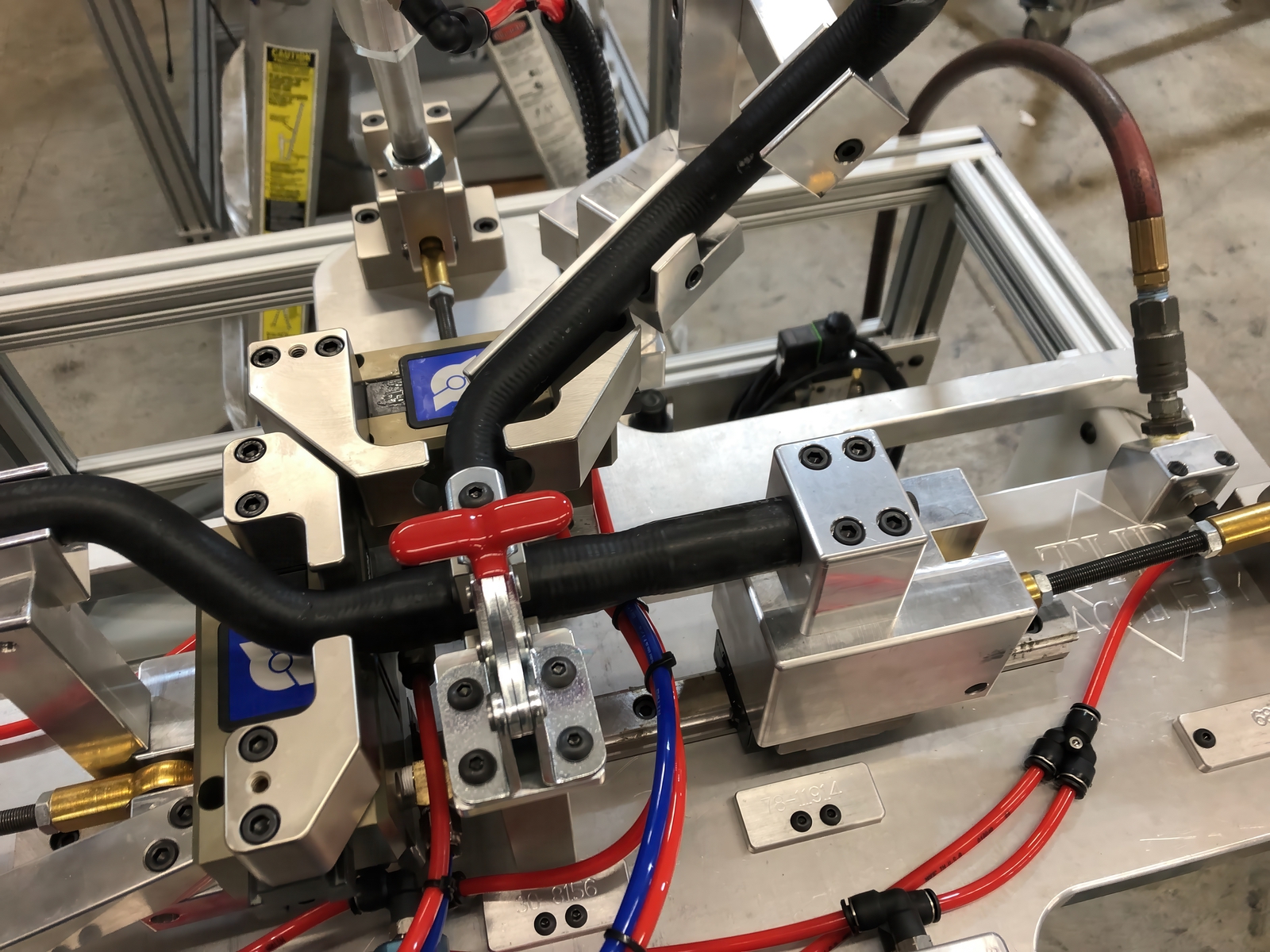 Close-up of an industrial machine frame with metal clamps, a red valve handle, and red/blue hydraulic hoses.