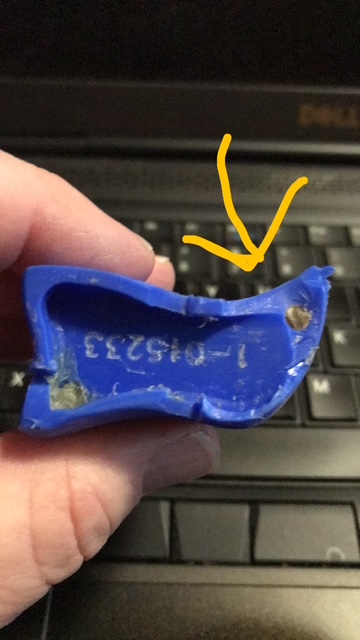 Close-up of a broken blue plastic device with a metal pin exposed, held between fingers over a laptop keyboard.