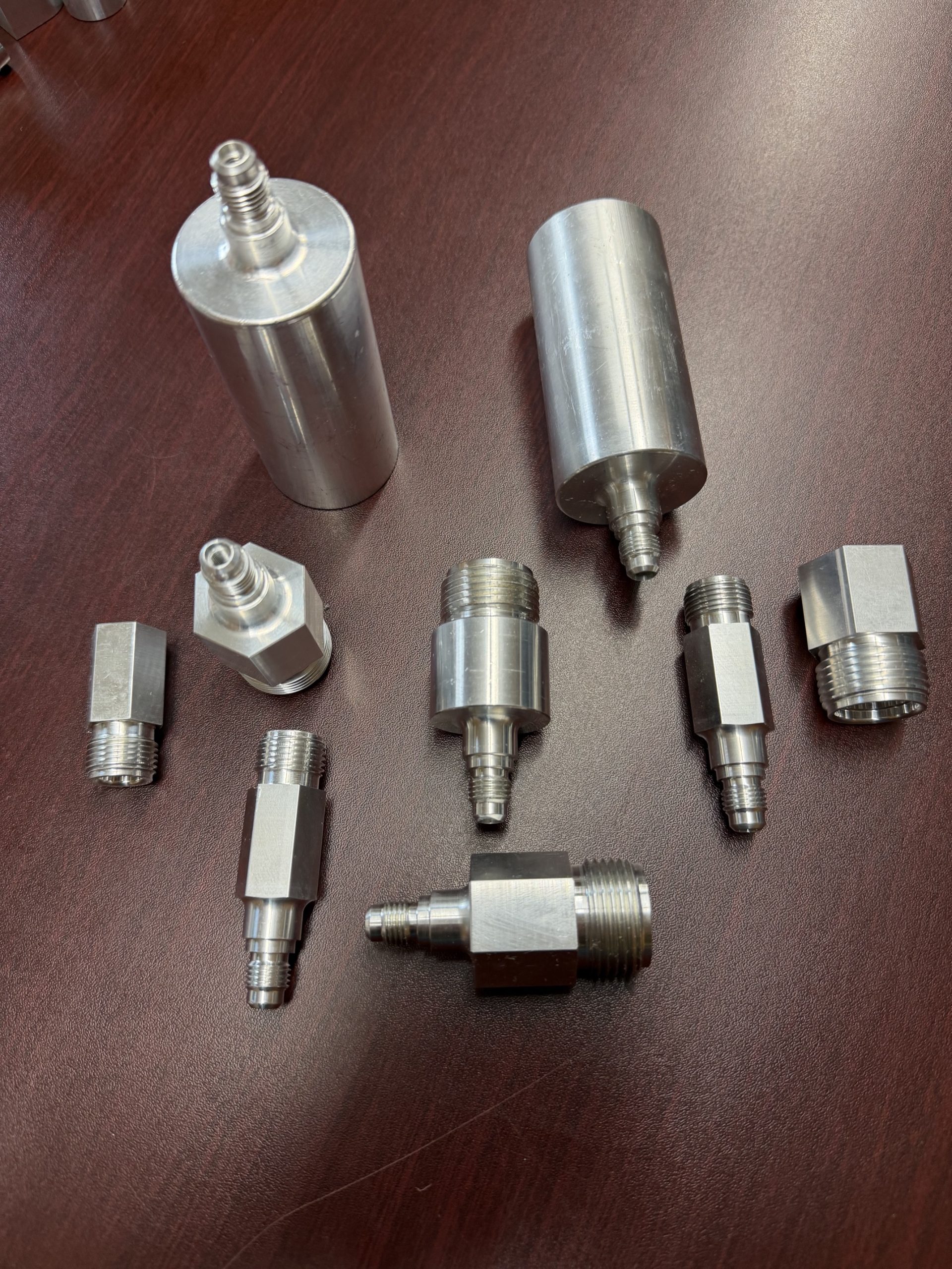 Assortment of metallic hydraulic fittings and adapters on a dark wooden surface.